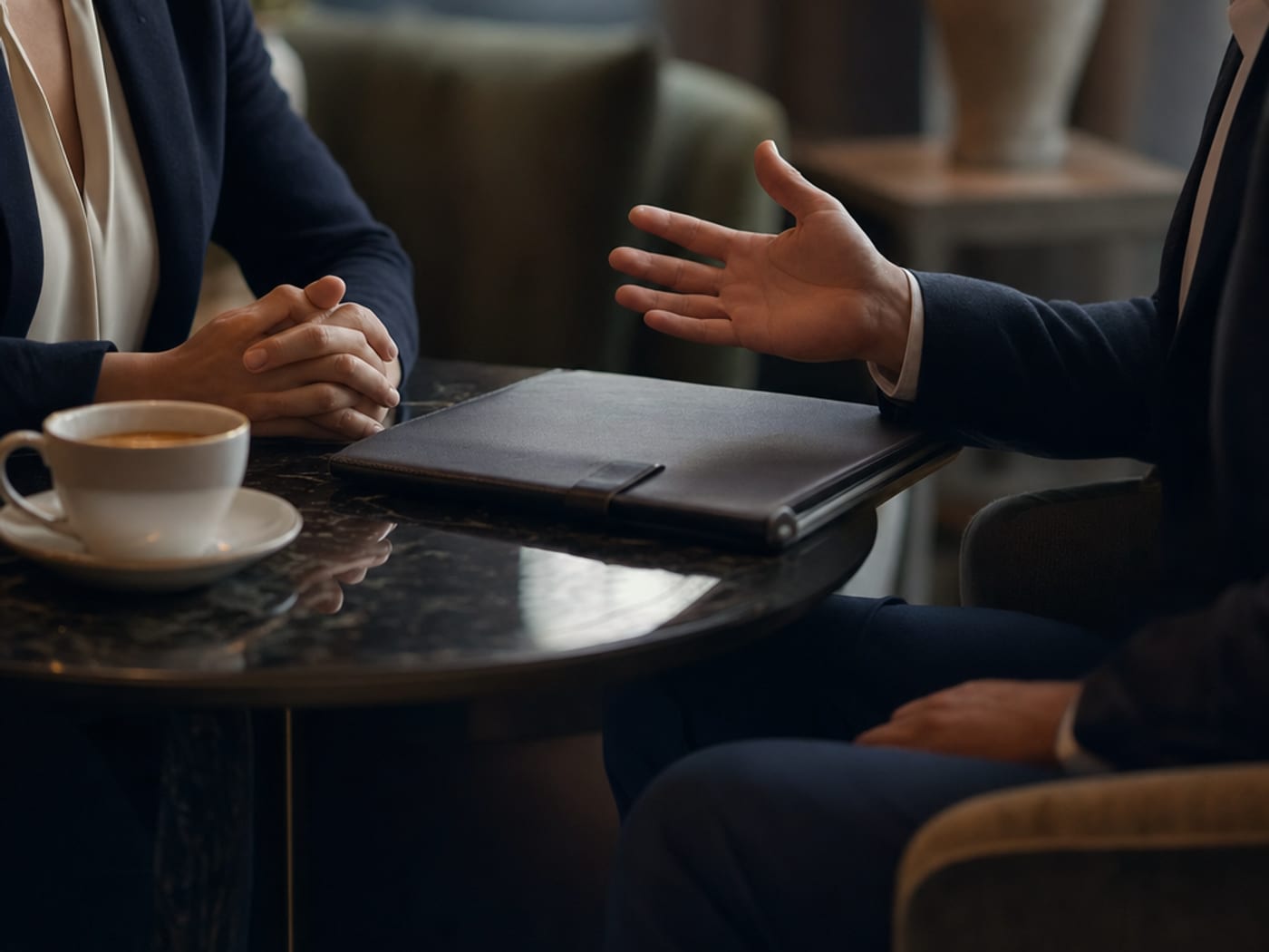 Two people in conversation across a table in a quiet hotel lounge.
